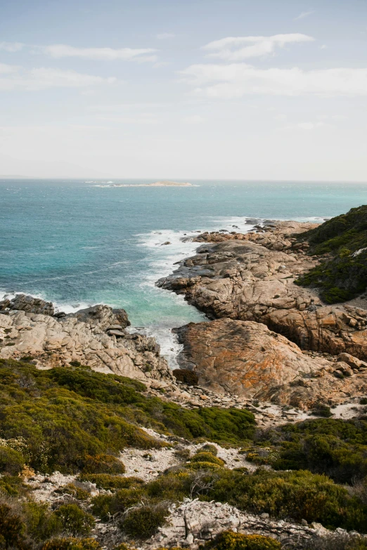 a view of the ocean from the top of a hill, rocky coast, “ iron bark, the emerald coast, granite