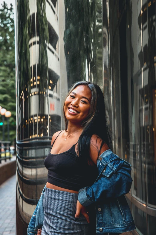 a woman standing in front of a tall building, large black smile, wearing a crop top, seattle, south east asian with round face