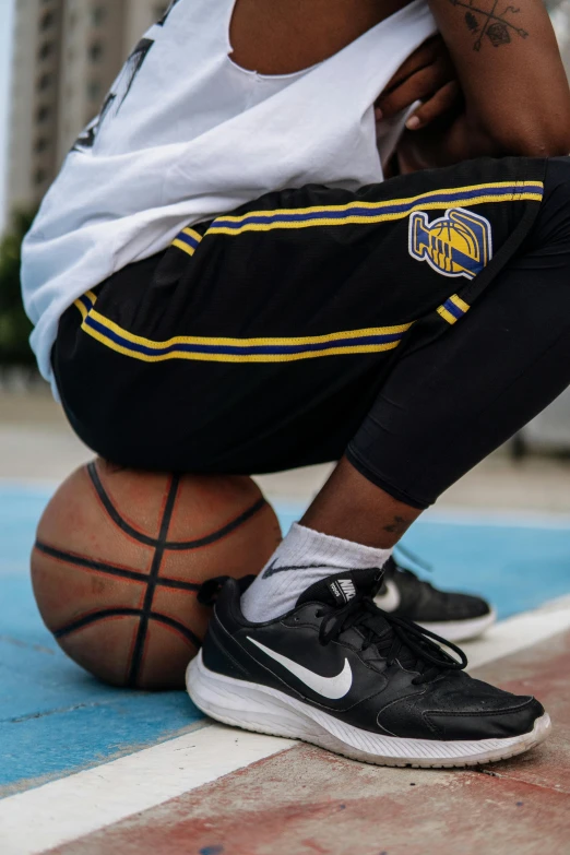 a man sitting on top of a basketball ball, black and yellow, leg and hip shot, zoomed in shots, street clothing