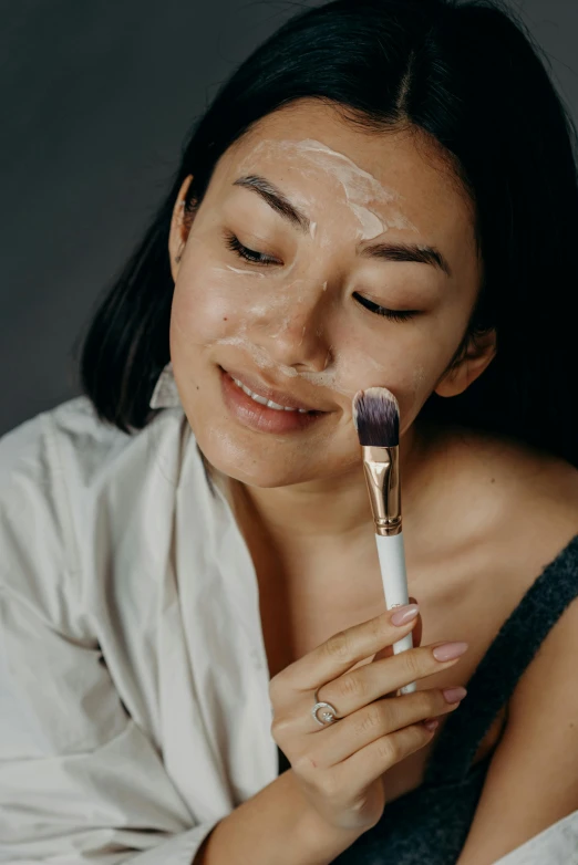 a woman that is holding a brush in her hand, trending on pexels, hyperrealism, face mask, malaysian, bubbling skin, textured base ; product photos