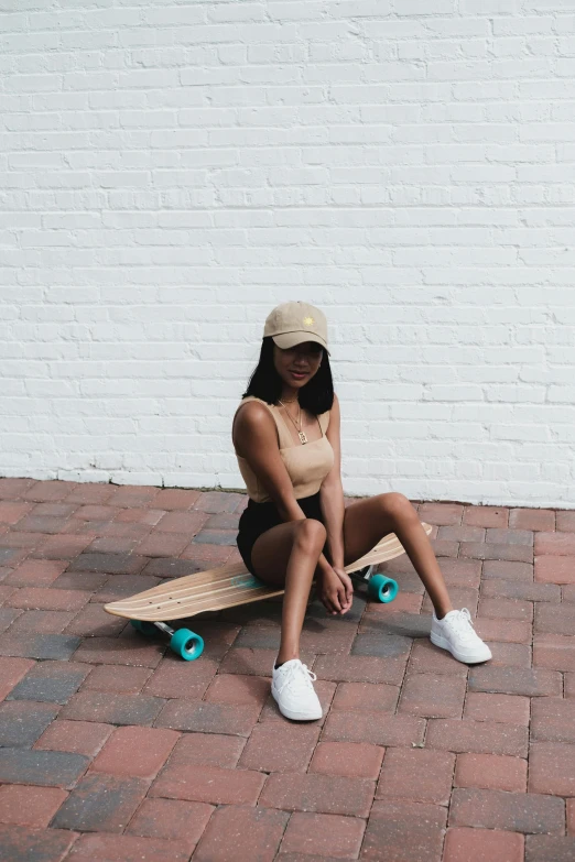 a woman sitting on a skateboard in front of a white brick wall, tan complexion, wearing crop top, white straw flat brimmed hat, trending on r/streetwear