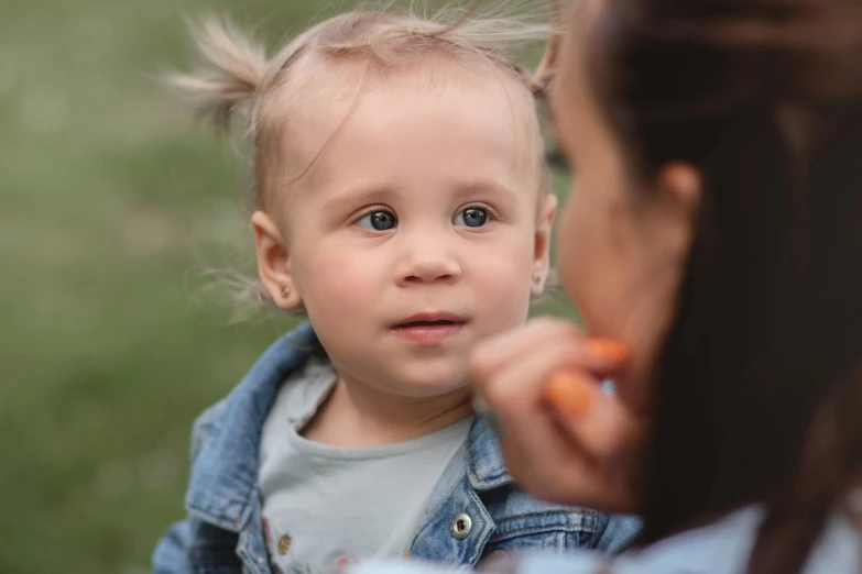 a woman holding a baby and brushing it's teeth, a picture, by Emma Andijewska, pexels contest winner, photorealism, at the park, small blond goatee, woman with braided brown hair, 2 years old