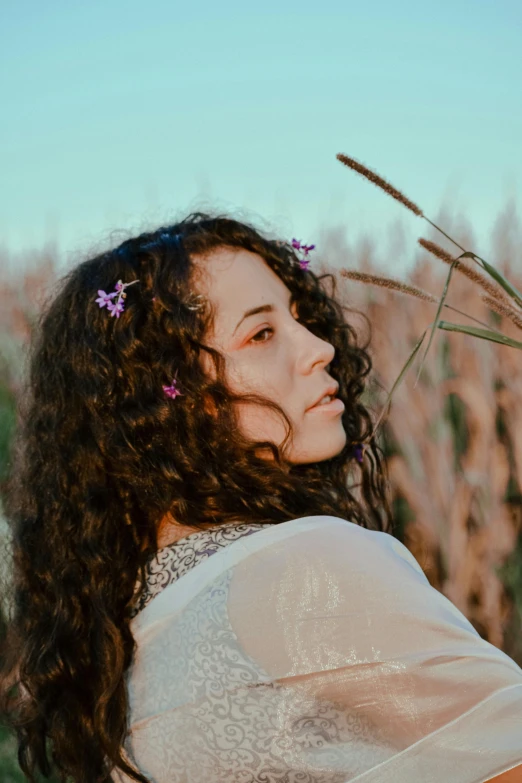 a woman standing in a field of tall grass, an album cover, pexels contest winner, renaissance, curly dark hair, flowers on hair, young middle eastern woman, profile pic