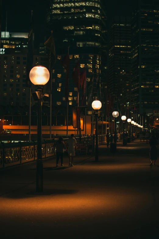 a group of people walking down a street at night, inspired by Sydney Carline, pexels contest winner, floor lamps, beside the river, in chippendale sydney, big beautiful street lamps