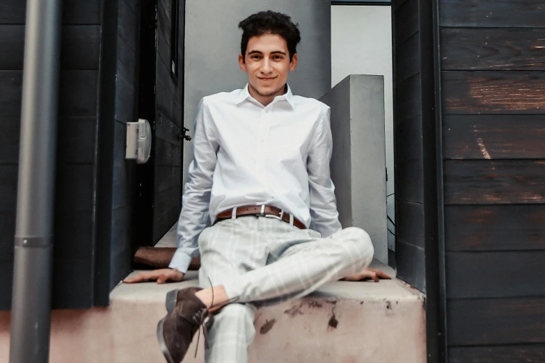 a man sitting on top of a cement block, an album cover, inspired by Alejandro Obregón, pexels contest winner, renaissance, wearing a white button up shirt, 14 yo berber boy, formal attire, relaxing and smiling at camera