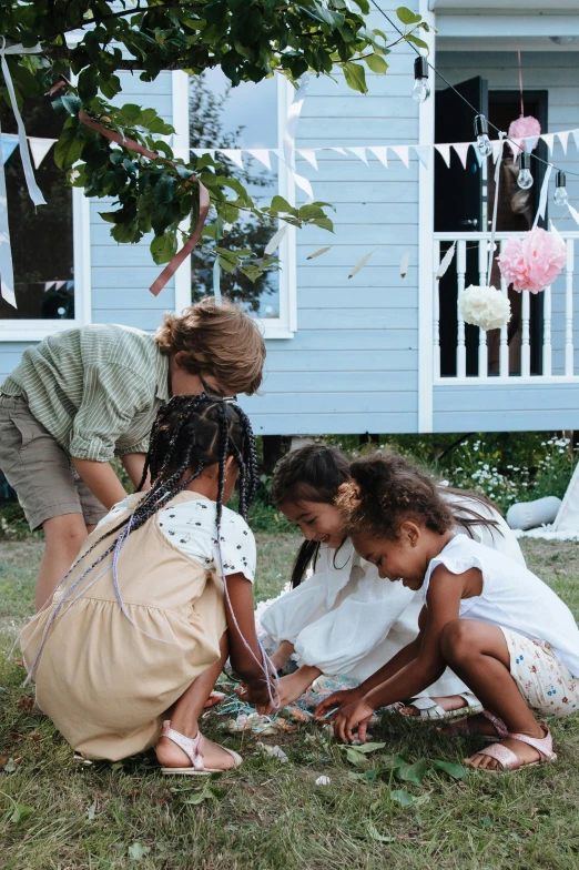 a group of children sitting on the grass in front of a house, hygge, confetti, midsommar style, grey