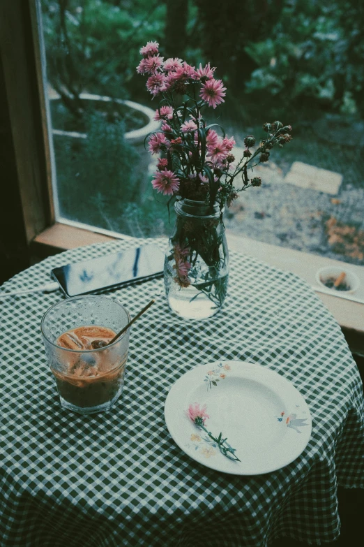 a table with a vase of flowers and a plate of food, inspired by Elsa Bleda, unsplash, realism, ice coffee, rainy day, low quality photo, old picture