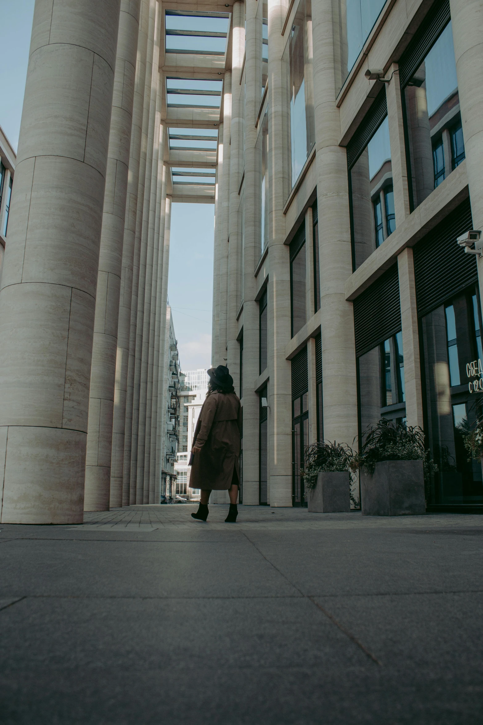 a woman walking down a sidewalk in front of a tall building, inspired by Ricardo Bofill, pexels contest winner, pillars of marble, cinematic paris, low quality photo, panoramic view of girl