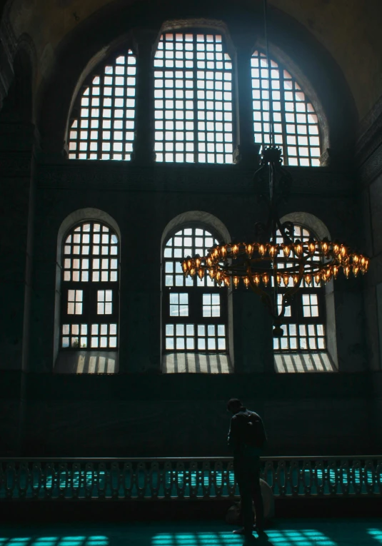 a person standing in front of a large window, inspired by Osman Hamdi Bey, unsplash contest winner, church chandelier, low quality photo, istanbul, crypt