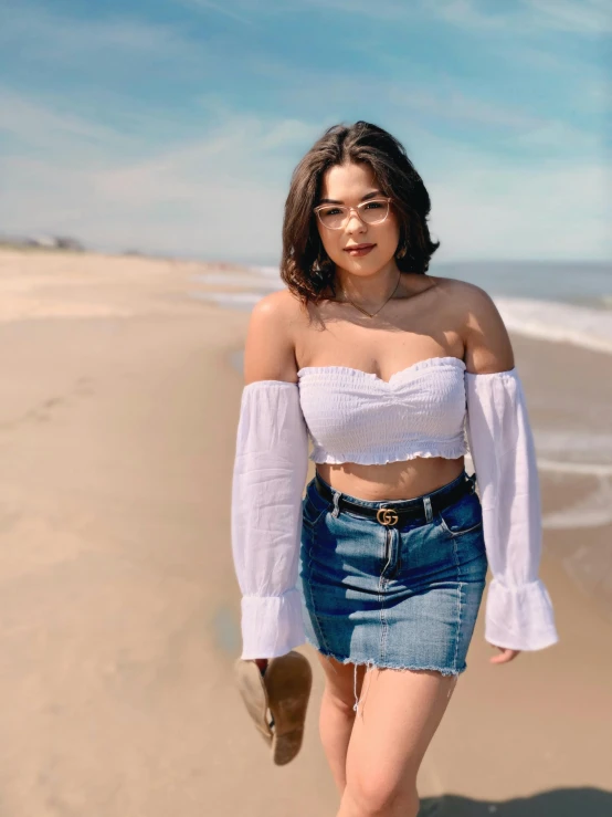 a woman standing on a beach next to the ocean, by Robbie Trevino, wearing a cropped top, wearing denim, white miniskirt, upper body image