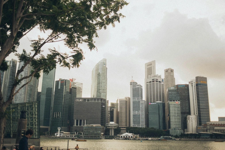 a group of people sitting on a bench next to a body of water, pexels contest winner, hyperrealism, the singapore skyline, brutalist office buildings, white buildings with red roofs, 2000s photo