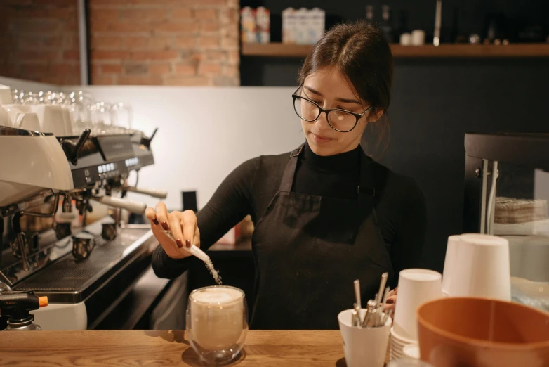 a woman standing in front of a coffee machine, trending on unsplash, sitting on a mocha-colored table, aussie baristas, low quality photo, wearing an apron