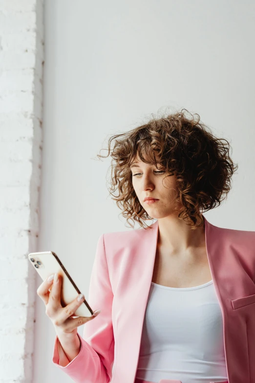 a woman in a pink jacket looking at her cell phone, trending on pexels, renaissance, brown curly hair, office clothes, human staring blankly ahead, instagram picture