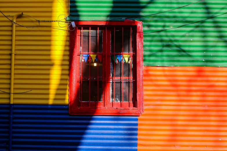 a yellow fire hydrant sitting in front of a colorful building, a photo, inspired by Steve McCurry, pexels contest winner, color field, wires hanging across windows, chilean, the sun reflecting on a window, colorful striped pavillions