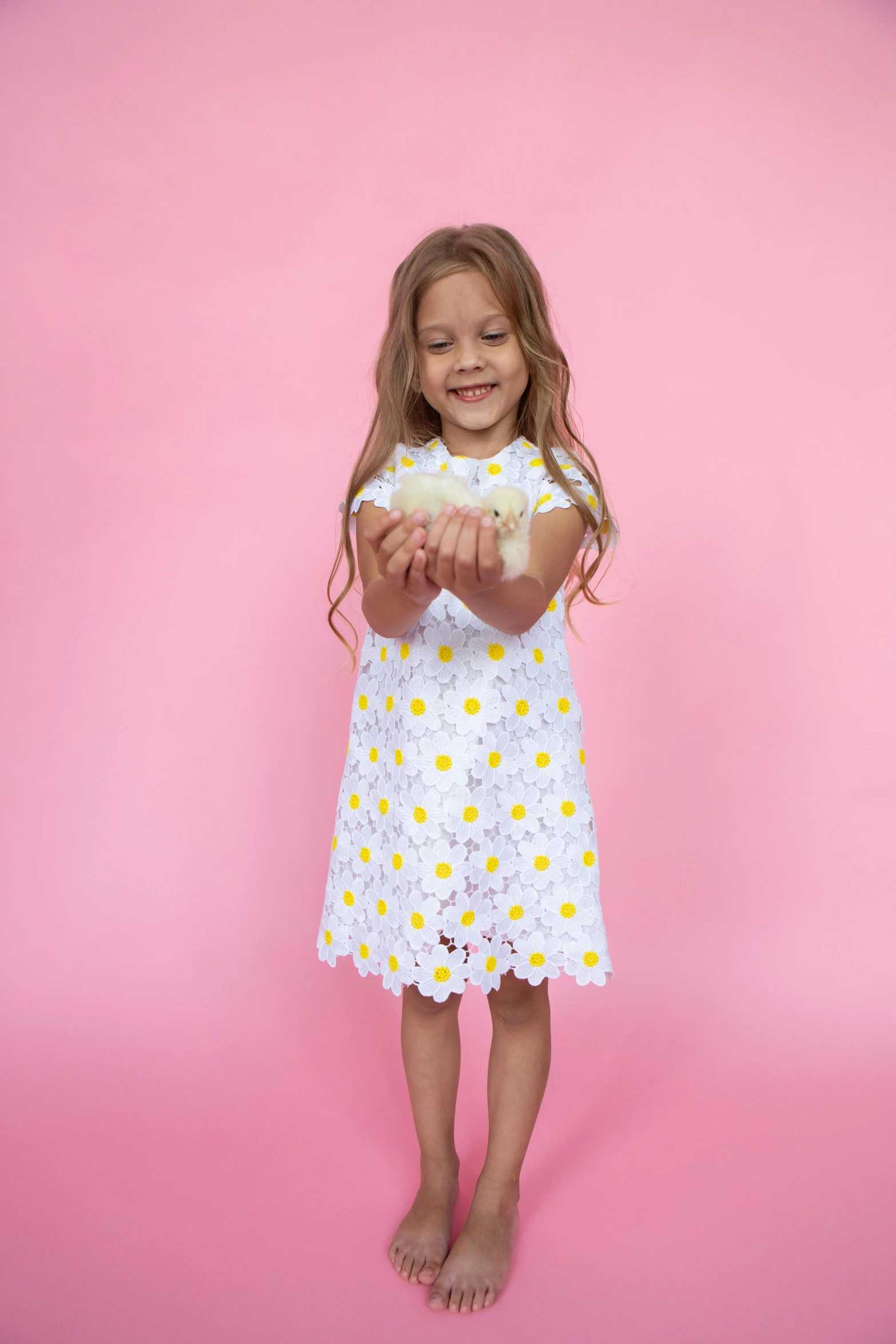 a little girl standing in front of a pink background, inspired by Annabel Kidston, shutterstock contest winner, holding daisy, 360 degree view, white and yellow scheme, wearing dresses