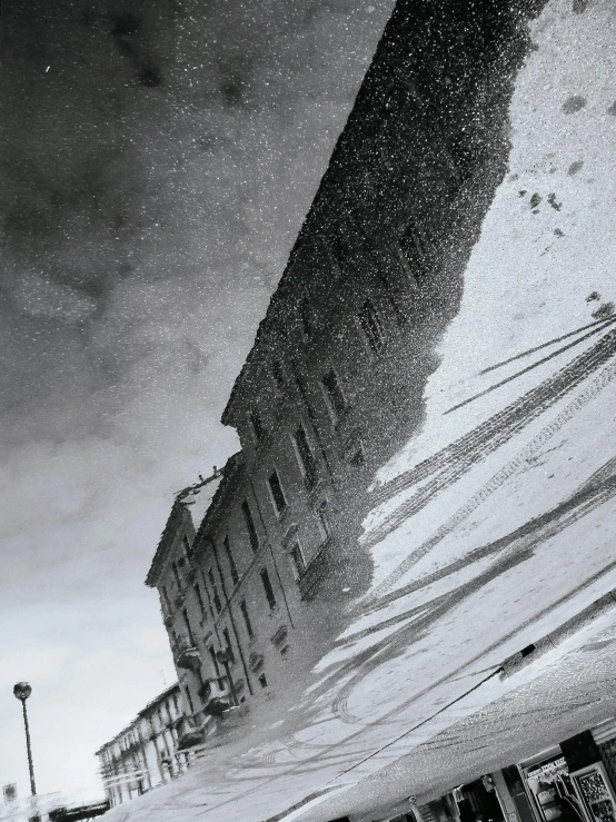 a reflection of a building in a puddle of water, an album cover, by Patrick Pietropoli, pexels contest winner, snowstorm ::5, view from below, historical photo, snowy italian road