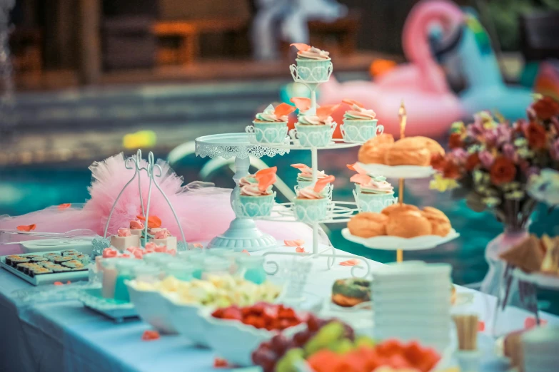 a table topped with lots of food next to a pool, a colorized photo, pexels contest winner, pink and teal and orange, cupcake, fairytale, background image