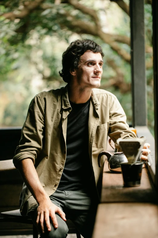 a man sitting on a bench with a cup of coffee, ben askren, portrait image, in sao paulo, plants