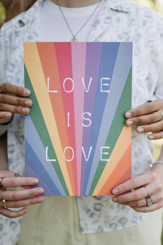 a woman holding a sign that says love is love, poster art, by Julia Pishtar, trending on pexels, greeting card, rainbows, couple, print on magazine