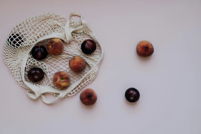 a bag of plums sitting on top of a table, by Emma Andijewska, pexels contest winner, red mesh in the facede, peach, white backdrop, background image