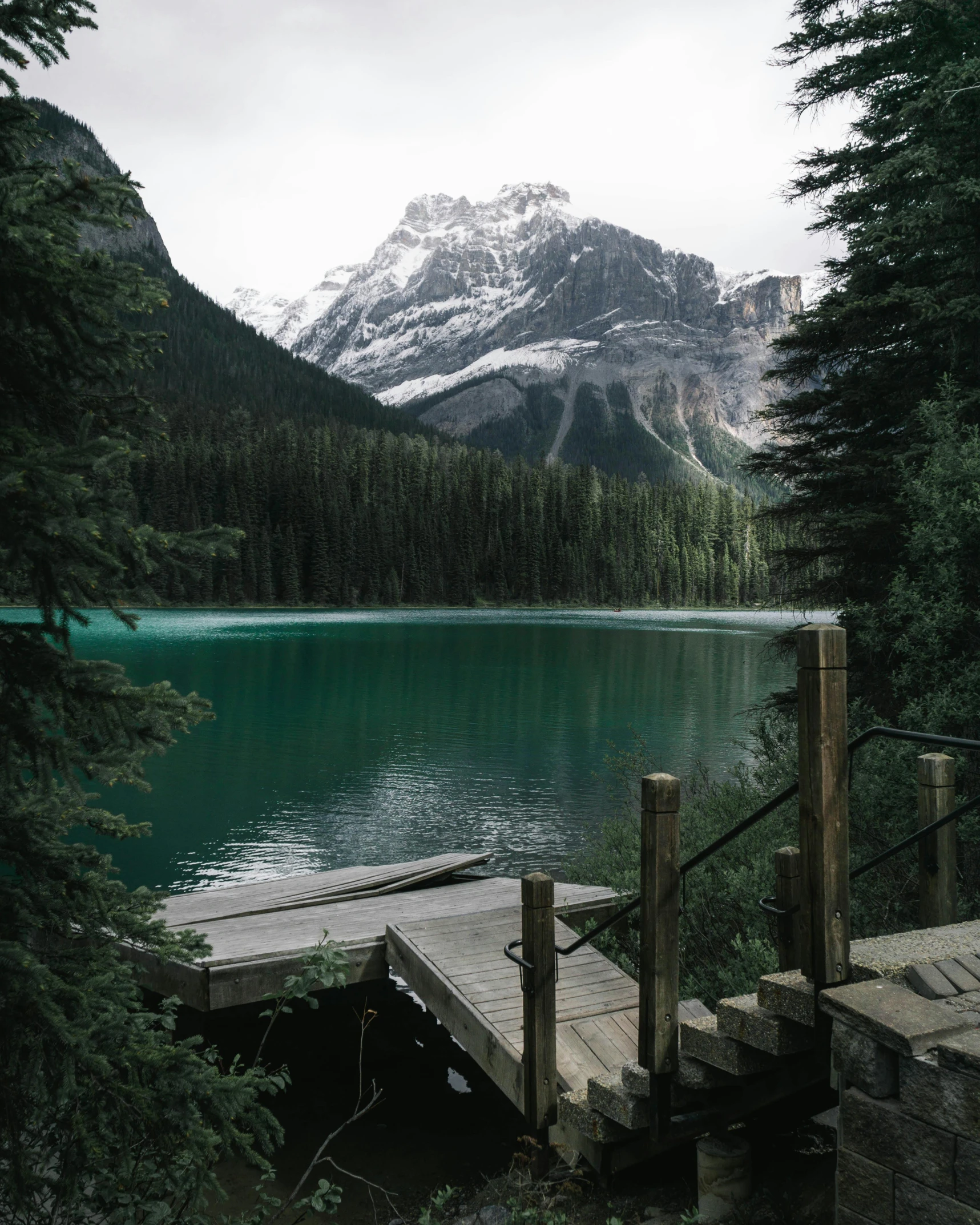 a dock next to a body of water with a mountain in the background, dark green water, banff national park, without duplicate image