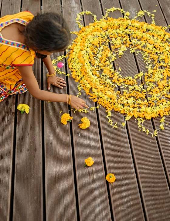 a little girl sitting on top of a wooden floor, inspired by Andy Goldsworthy, pexels contest winner, kalighat flowers, colors: yellow, made of flowers, sri lanka