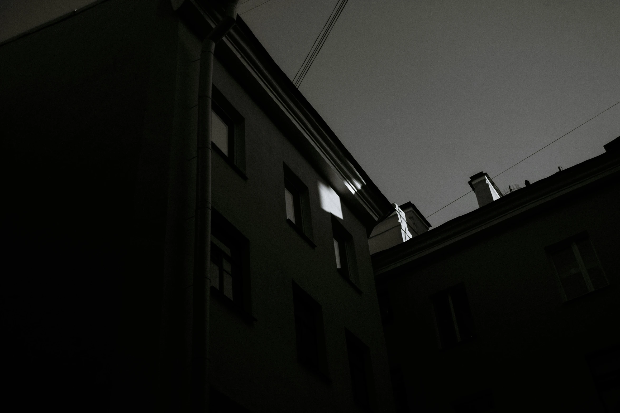 a black and white photo of a tall building, a black and white photo, by Tamas Galambos, pexels contest winner, light and space, in an alley at night back lit, the glow of the moonlight, attached to wires. dark, anna nikonova