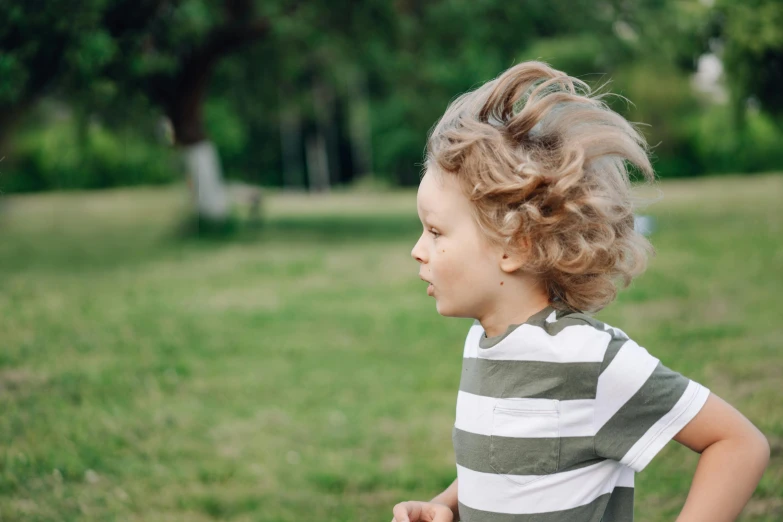 a little boy standing on top of a lush green field, pexels contest winner, happening, her hair blowing in the wind, looking to his side, short light grey whiskers, in a park