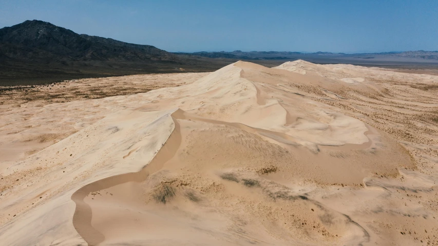 sand dunes in the desert with mountains in the background, unsplash contest winner, nazare (portugal), wide aerial shot, no foliage, australian desert