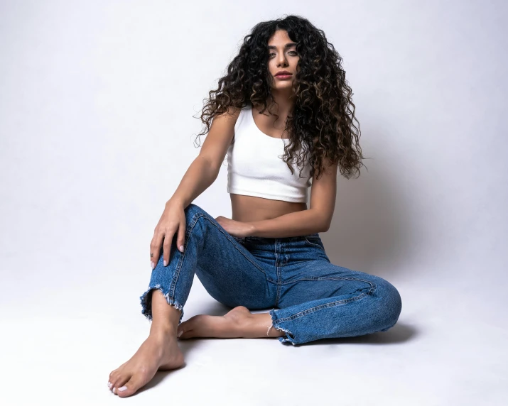 a woman sitting on the ground with her legs crossed, trending on pexels, renaissance, outfit : jeans and white vest, curly haired, young middle eastern woman, wearing a crop top