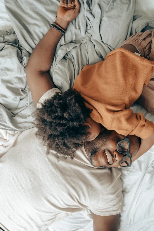 a man and woman laying in bed next to each other, by Jessie Algie, trending on pexels, with afro, motherly, hugs, top down shot