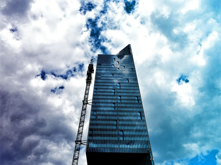 a tall building with a crane in front of it, by Sebastian Spreng, pexels contest winner, constructivism, covered in clouds, thumbnail, high definition photo, low angle!!!!