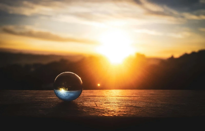 a glass ball sitting on top of a wooden table, unsplash, refracted sunset, transparent droplets, instagram post, sun set