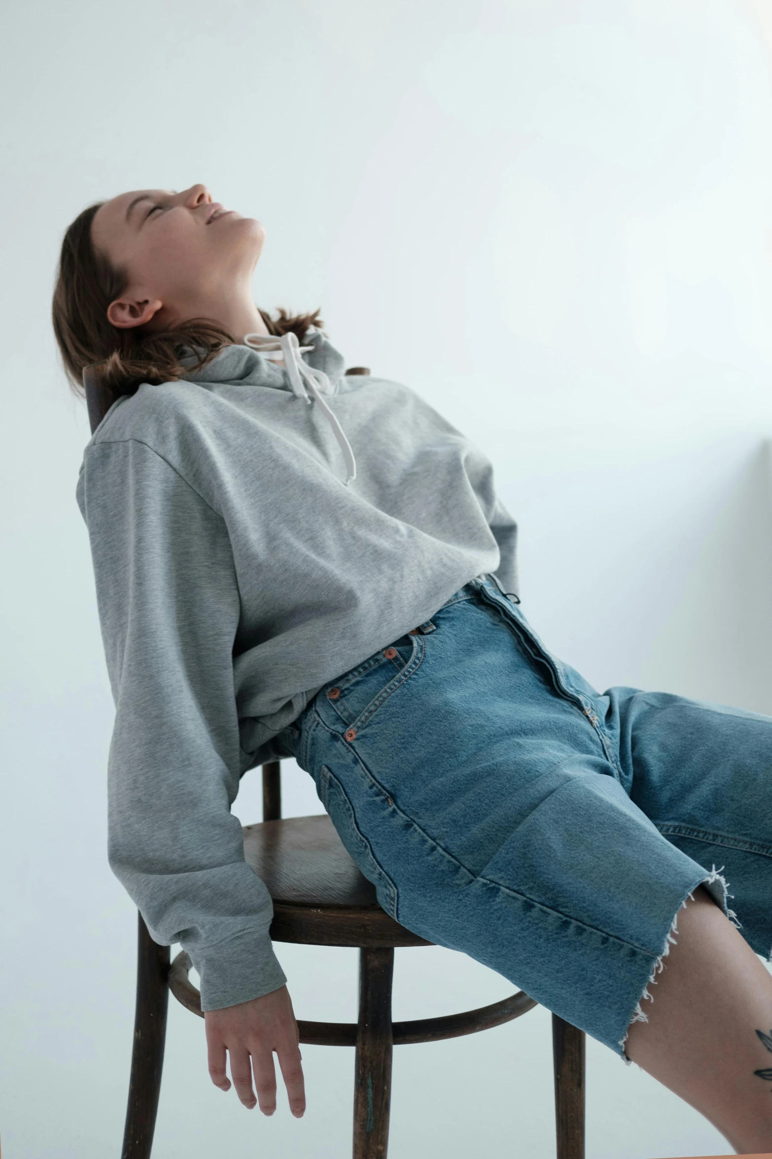 a woman sitting on top of a wooden chair, inspired by Sarah Lucas, trending on unsplash, renaissance, gray hoodie, denim short pants, portrait of a woman sleeping, head tilted downward