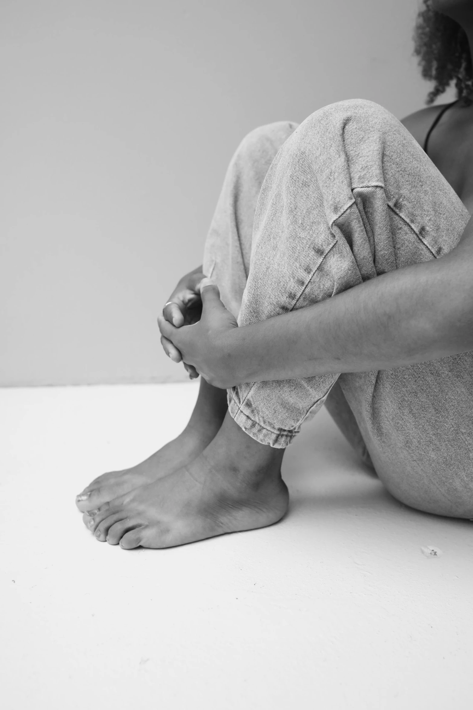 a black and white photo of a woman sitting on the floor, pexels, hyperrealism, ( ( ( wearing jeans ) ) ), focus on his foot, plain background, clinically depressed