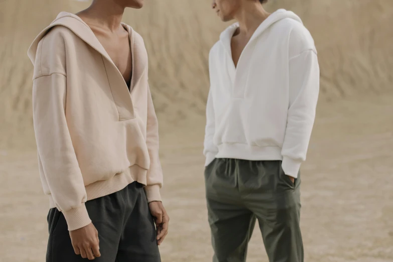 a couple of men standing next to each other, inspired by Louis Hersent, trending on pexels, beige hoodie, open v chest clothes, on the sand, wearing acne outfit