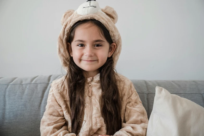 a little girl sitting on a couch wearing a teddy bear costume, a cartoon, inspired by Maurice Sendak, pexels contest winner, hurufiyya, brunette, beige, manuka, wearing a track suit