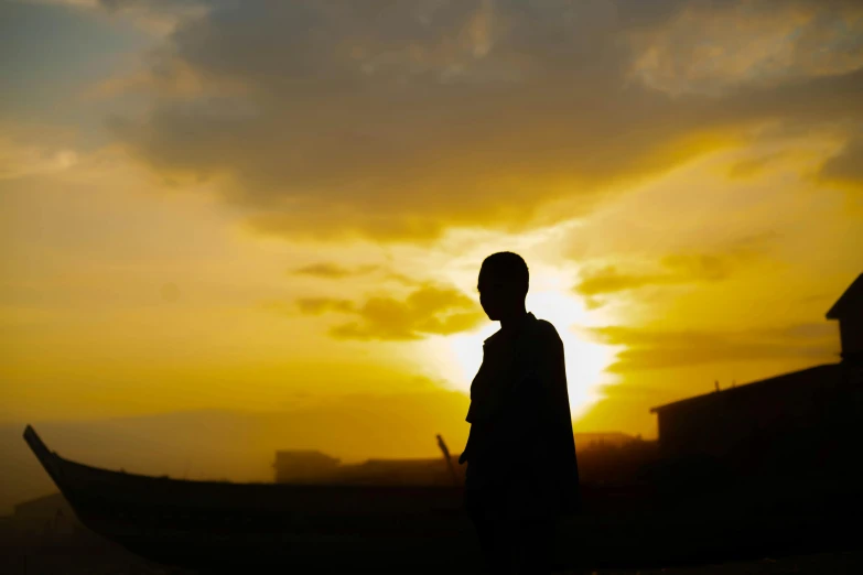 a person standing in front of a boat at sunset, pexels contest winner, happening, unmistakably kenyan, teenage boy, silhouette :7, yellow sky