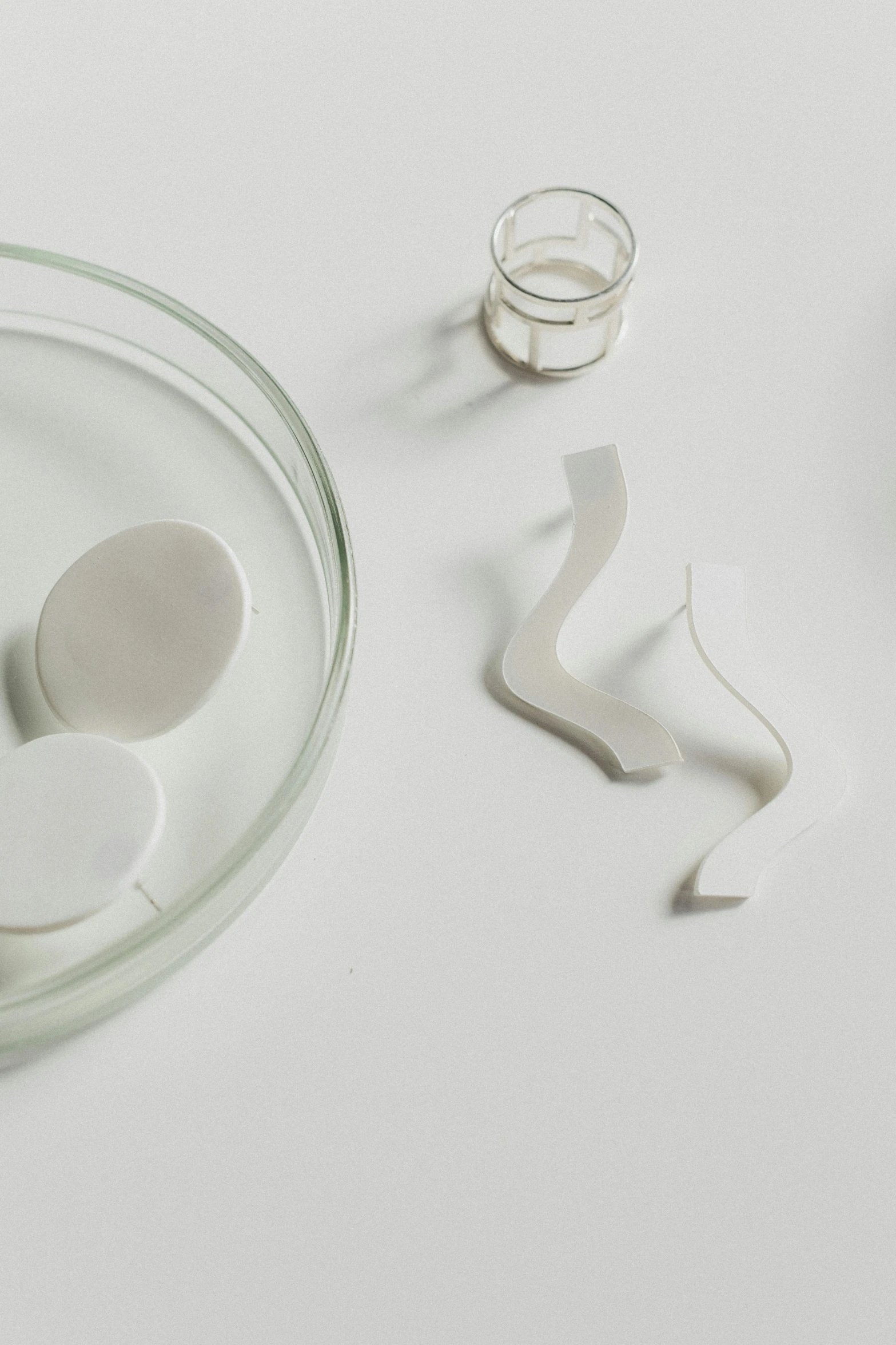 a glass bowl sitting on top of a white table, an abstract sculpture, inspired by Isamu Noguchi, trending on unsplash, 2 d lasercut earrings, detail shot, smooth and clean vector curves, pills