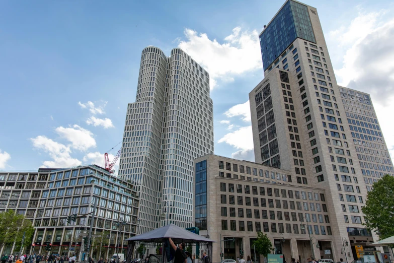 a group of people walking down a street next to tall buildings, bauhaus, two organic looking towers, berlin, capital plaza, exterior photo