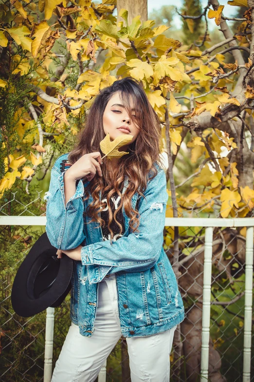 a woman standing in front of a fence eating a banana, pexels contest winner, hailee steinfeld, wearing a jeans jackets, covered in leaves, beautiful iranian woman