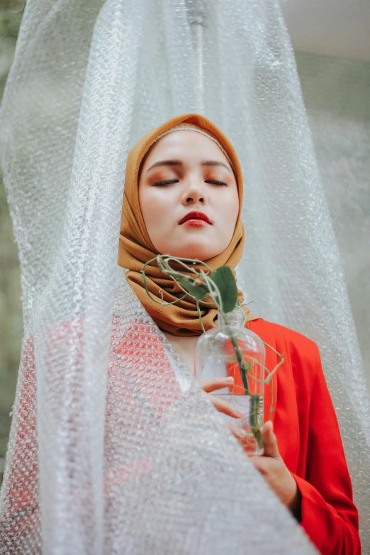 a woman wearing a hijab holding a flower, a picture, pexels contest winner, aestheticism, white and orange, portrait of modern darna, floating in perfume, with a straw