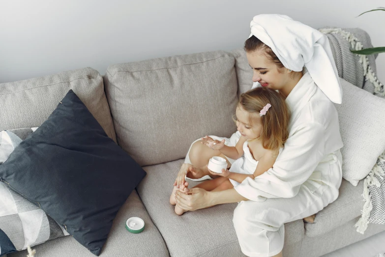 a woman and a little girl sitting on a couch, skincare, wearing a grey robe, profile image, from the elbow