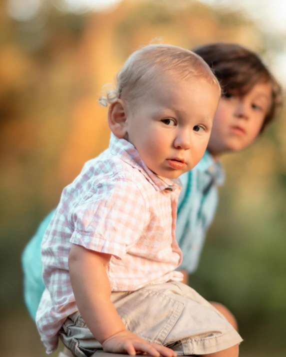 a little boy sitting on top of a wooden post, by Elizabeth Durack, unsplash, happening, two handsome men, dappled in evening light, lovingly looking at camera, putti