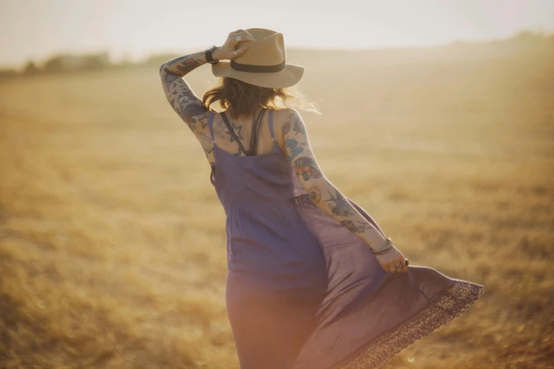 a woman in a dress and hat standing in a field, by Jessie Algie, trending on pexels, symbolism, with tattoos, late summer evening, various posed, a woman walking