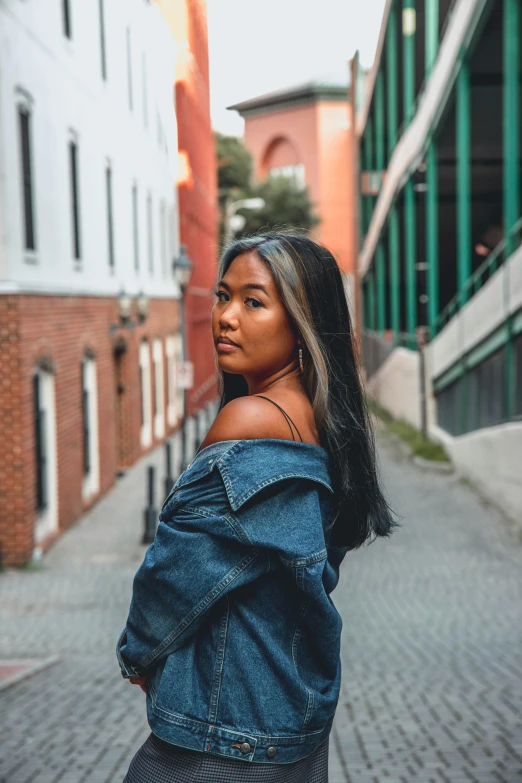 a woman standing in the middle of a street, inspired by helen huang, trending on unsplash, realism, wearing a jeans jackets, with brown skin, proud looking away, asian features