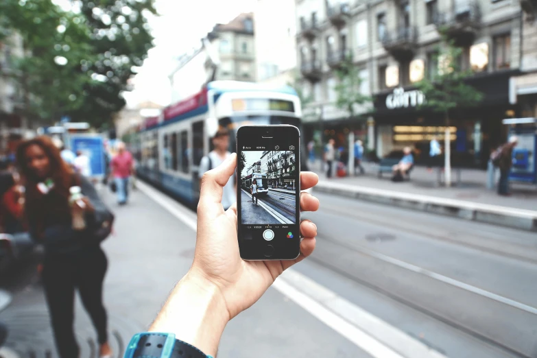 a person taking a picture of a street with a cell phone, by Niko Henrichon, pexels contest winner, photorealism, mobile learning app prototype, holding it out to the camera, vintage photo, with a long