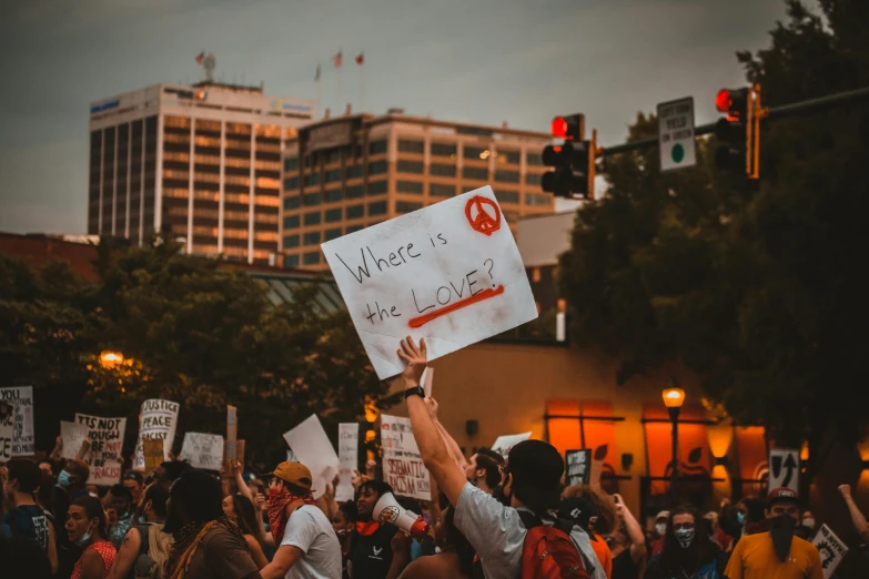 a man holding a sign in the middle of a crowd, a photo, trending on pexels, graffiti, background image, summer evening, protesters holding placards, lovecratian