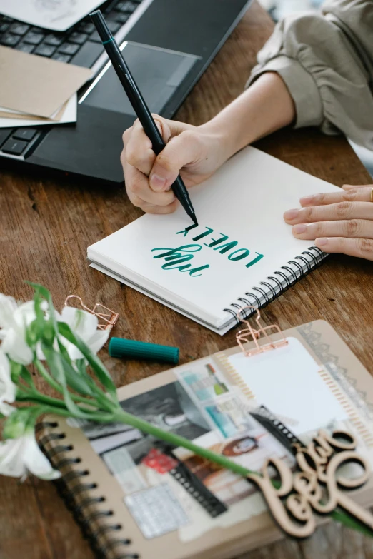 a woman sitting at a table writing on a notebook, a picture, trending on pexels, visual art, flowing lettering, flat lay, low quality photo, inspect in inventory image