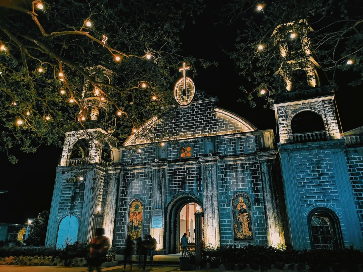 a church lit up at night with string lights, by Robbie Trevino, pexels contest winner, baroque, 1970s philippines, city lights made of lush trees, front facing view, well preserved